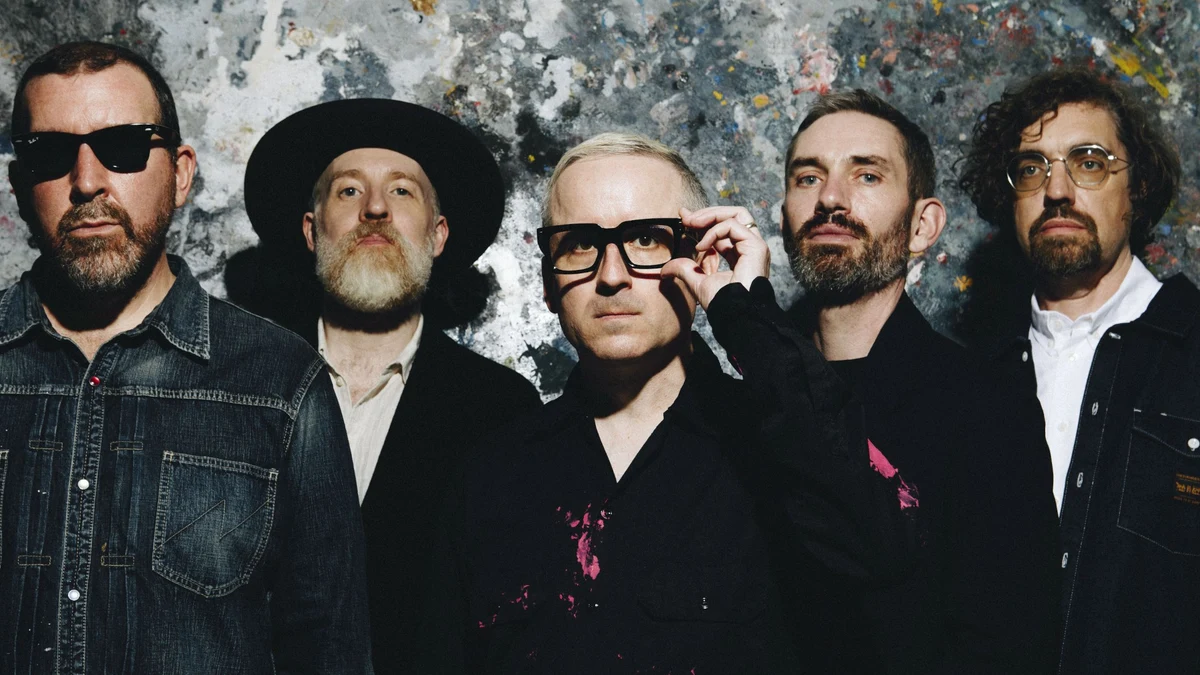 The five members of Hot Chip standing against a paint-splattered wall.